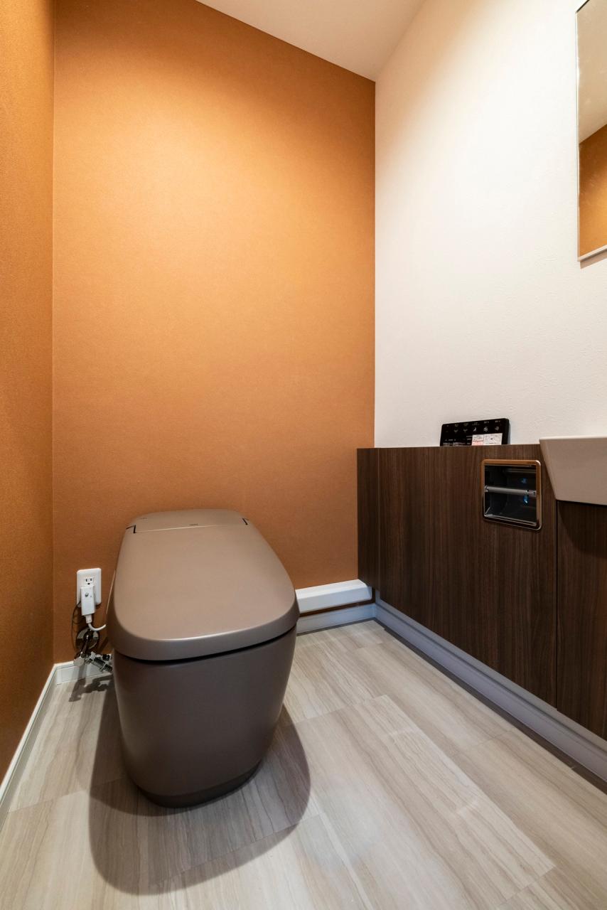 アイコニックなオレンジ色のクロスに馴染むブラウンのトイレはLIXILのサティス